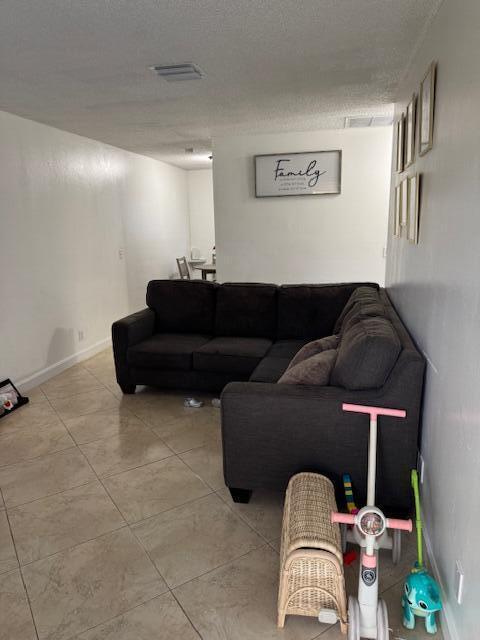 living room featuring light tile patterned floors, a textured ceiling, visible vents, and baseboards