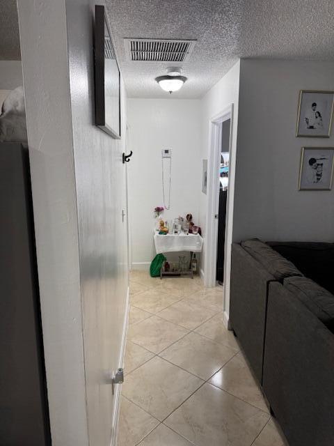 hall featuring a textured ceiling, light tile patterned floors, visible vents, and baseboards