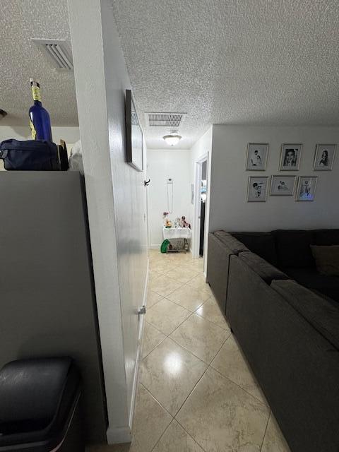 hall with a textured ceiling, light tile patterned floors, and visible vents