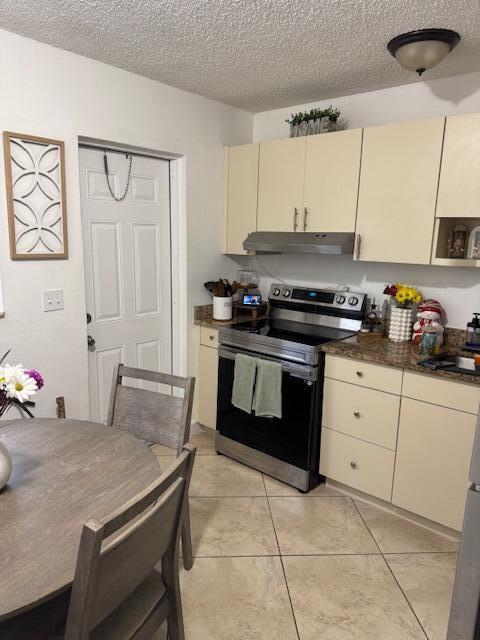 kitchen with dark countertops, stainless steel electric range oven, cream cabinets, a textured ceiling, and under cabinet range hood