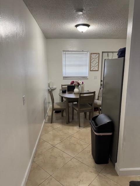 dining space with a textured ceiling, light tile patterned floors, and baseboards