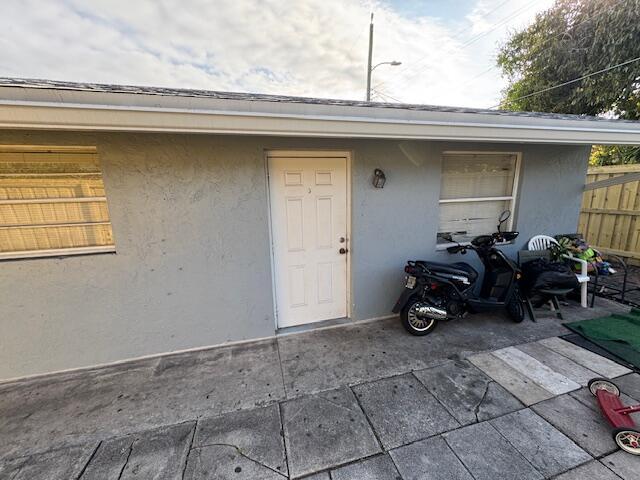 view of exterior entry with stucco siding, fence, and a patio