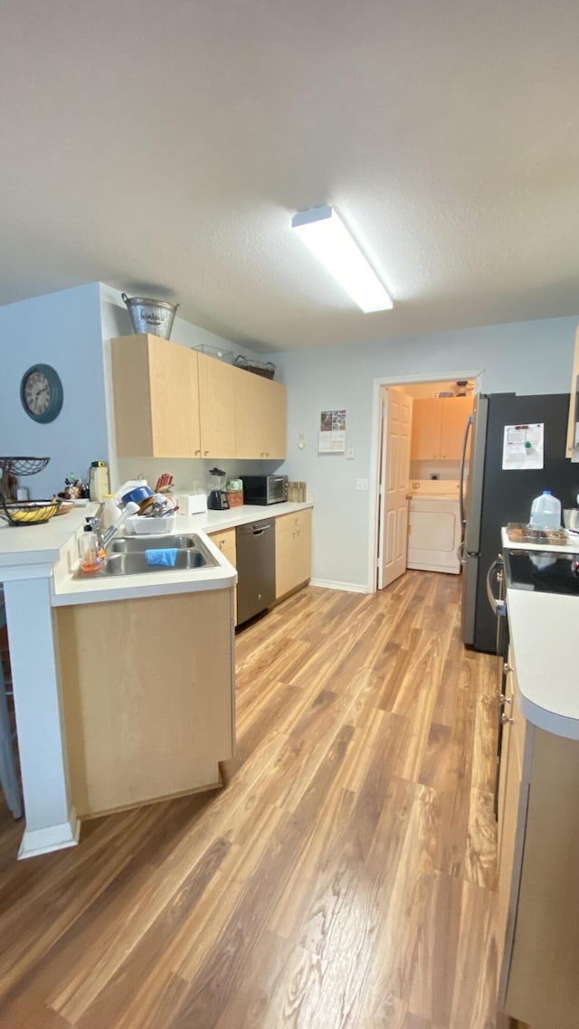 kitchen with stainless steel appliances, washer / clothes dryer, light countertops, a sink, and light wood-type flooring