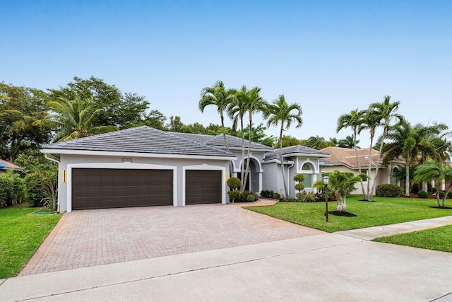 view of front of property featuring decorative driveway, stucco siding, a front yard, a garage, and a tiled roof