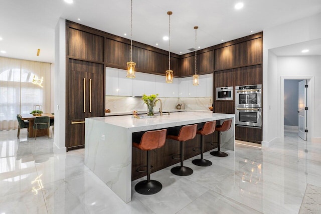 kitchen with double oven, marble finish floor, hanging light fixtures, backsplash, and a kitchen bar