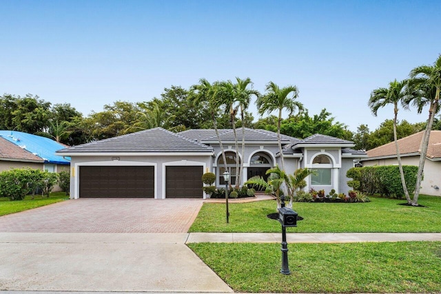 view of front of home featuring a garage, a tile roof, decorative driveway, stucco siding, and a front lawn