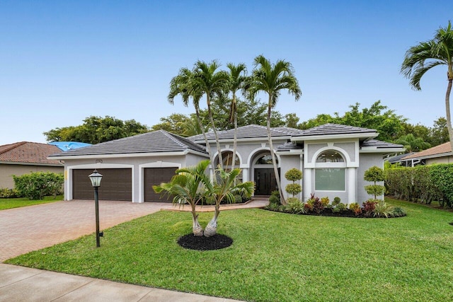 view of front of home with a garage, a tile roof, decorative driveway, stucco siding, and a front yard