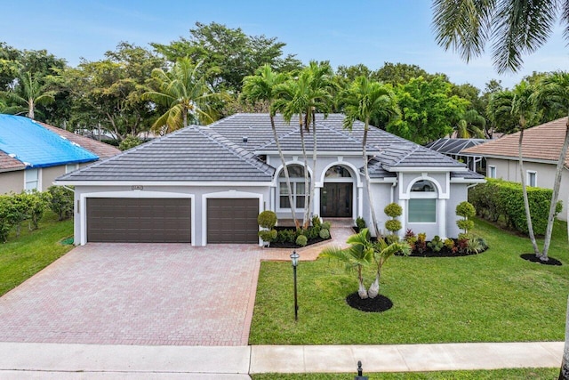 view of front of property featuring a garage, a tile roof, decorative driveway, a front yard, and stucco siding