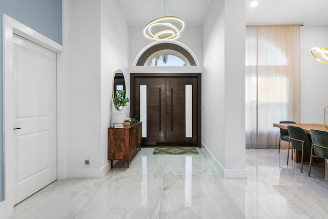 foyer entrance with marble finish floor, a high ceiling, baseboards, and an inviting chandelier