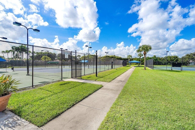 view of tennis court with a yard and fence