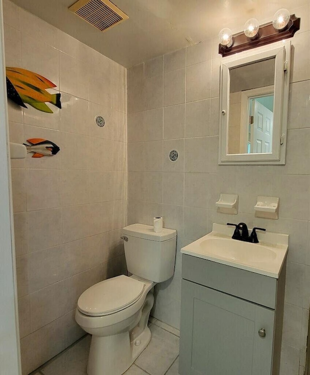 bathroom with visible vents, toilet, tile patterned floors, vanity, and tile walls