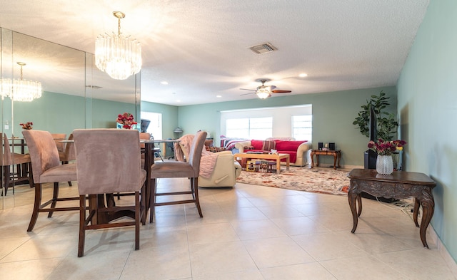 dining area featuring light tile patterned flooring, visible vents, a textured ceiling, and ceiling fan with notable chandelier