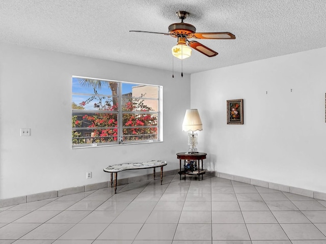 sitting room featuring ceiling fan, a textured ceiling, light tile patterned flooring, and baseboards