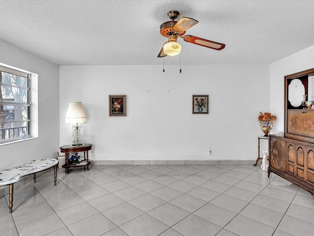 sitting room with light tile patterned floors, baseboards, a ceiling fan, and a textured ceiling