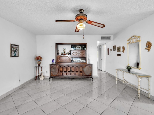 interior space featuring light tile patterned floors, ceiling fan, a textured ceiling, visible vents, and baseboards