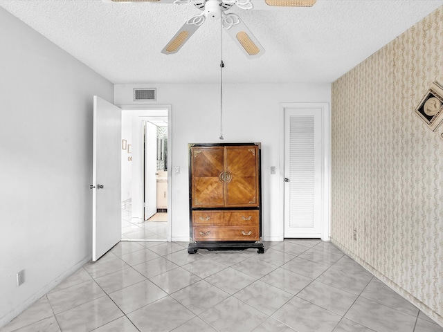 empty room featuring wallpapered walls, ceiling fan, visible vents, and a textured ceiling