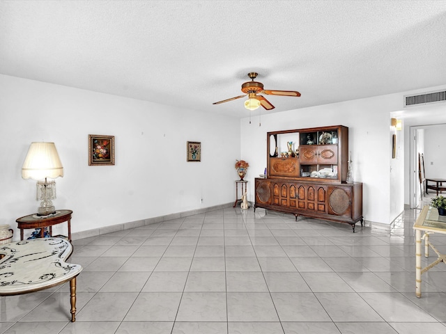 living area featuring a ceiling fan, a textured ceiling, baseboards, and light tile patterned floors