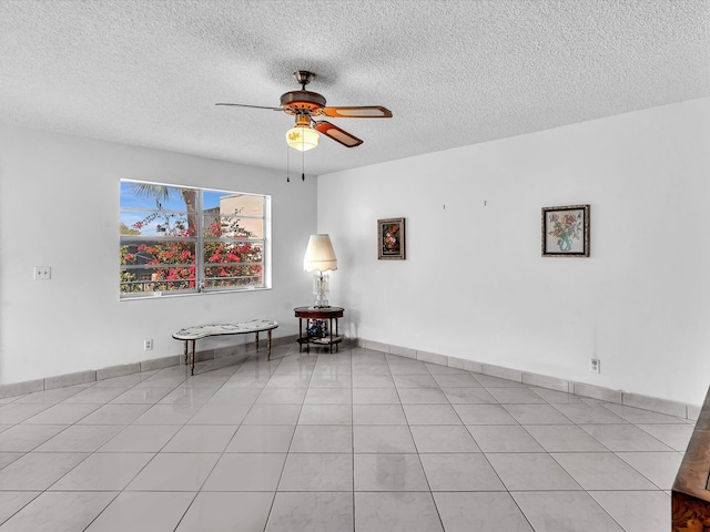 spare room featuring light tile patterned floors, ceiling fan, baseboards, and a textured ceiling