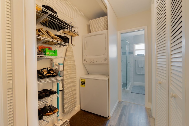 washroom featuring laundry area, baseboards, wood finished floors, and stacked washer and clothes dryer