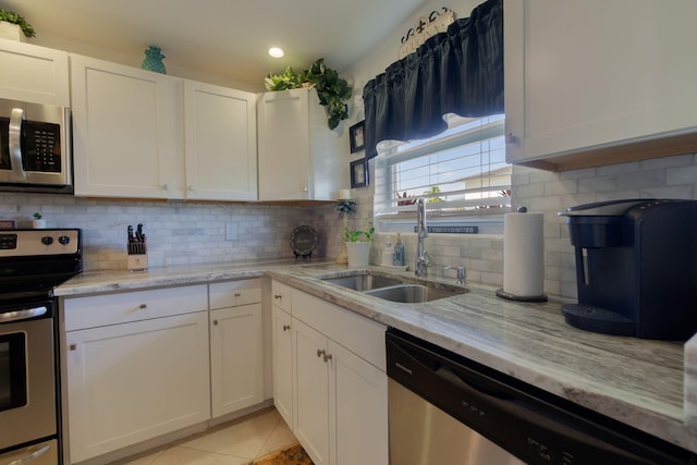 kitchen featuring stainless steel appliances, light tile patterned flooring, a sink, and white cabinetry