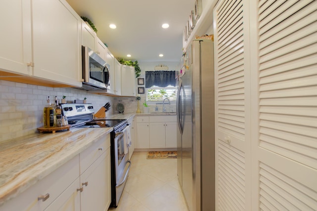 kitchen with light tile patterned floors, stainless steel appliances, a sink, white cabinets, and tasteful backsplash