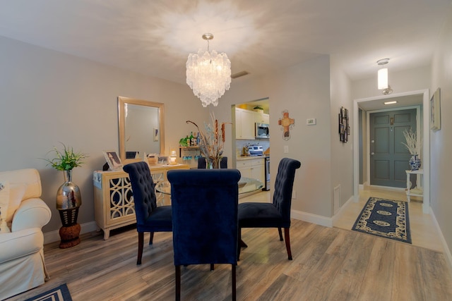 dining area featuring light wood finished floors, baseboards, visible vents, and a chandelier