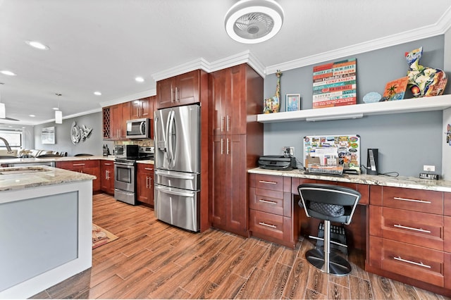 kitchen with appliances with stainless steel finishes, light stone counters, wood finished floors, crown molding, and built in desk