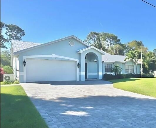 single story home featuring a garage, a front lawn, decorative driveway, and stucco siding