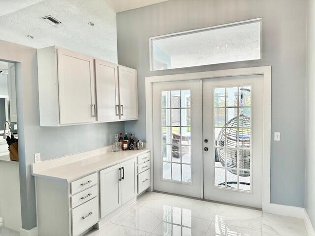 doorway featuring a textured ceiling, visible vents, baseboards, marble finish floor, and french doors