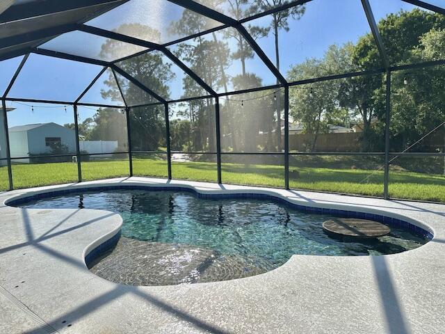 outdoor pool with glass enclosure, a yard, and a patio