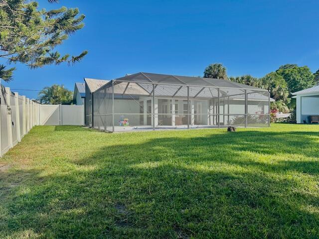 rear view of house featuring glass enclosure, a fenced backyard, and a lawn