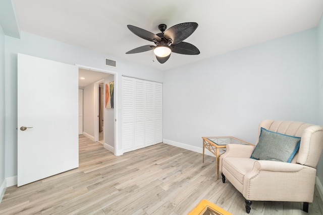 living area with light wood-style flooring, visible vents, baseboards, and a ceiling fan