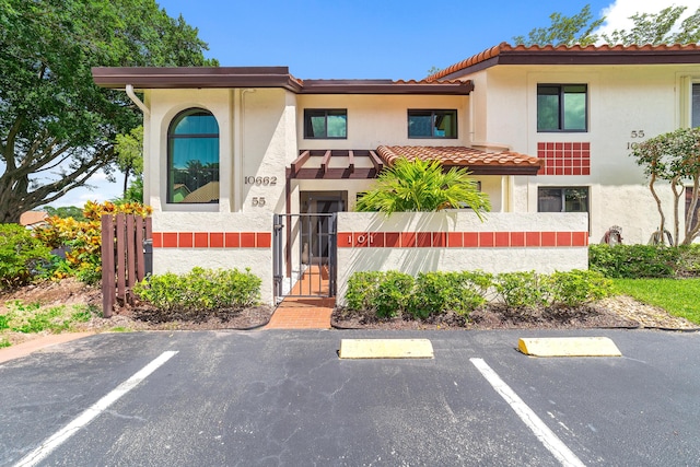 view of front facade with a fenced front yard, a tile roof, stucco siding, uncovered parking, and a gate