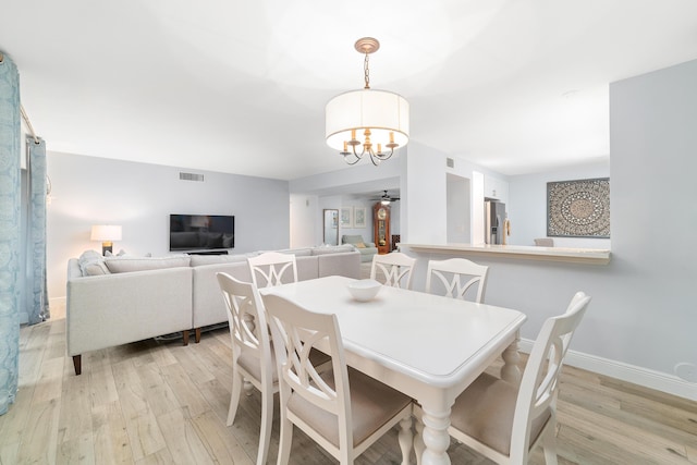 dining space with ceiling fan with notable chandelier, light wood-style flooring, visible vents, and baseboards