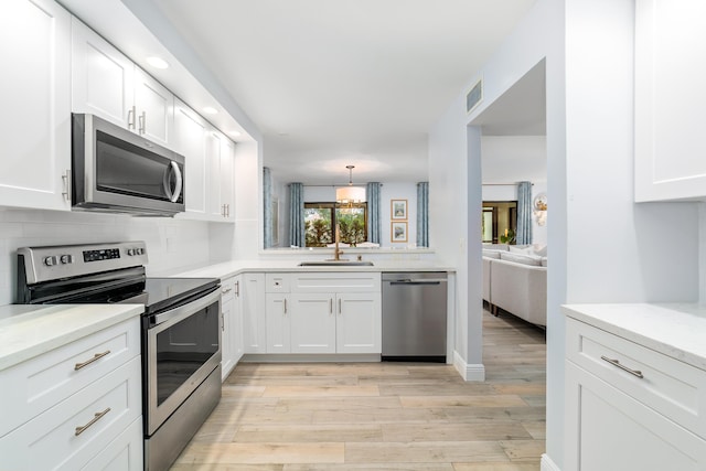 kitchen with a sink, visible vents, appliances with stainless steel finishes, backsplash, and light wood finished floors