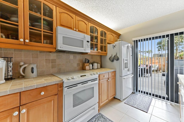 kitchen with light tile patterned floors, tasteful backsplash, glass insert cabinets, a textured ceiling, and white appliances