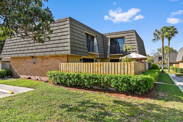 view of front of house featuring a front yard, brick siding, fence, and mansard roof