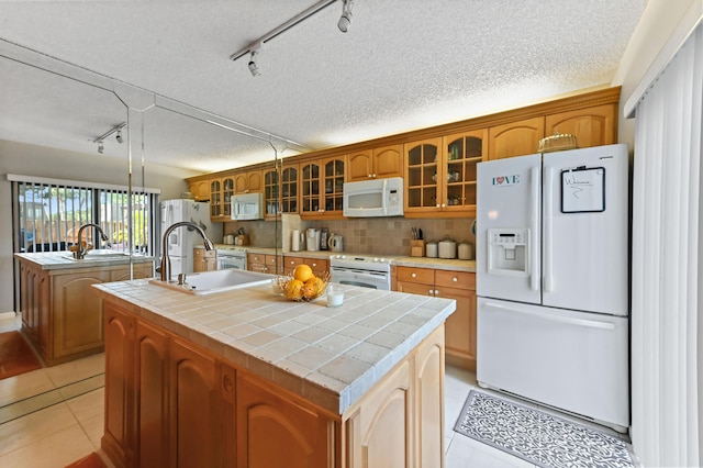 kitchen featuring white appliances, light tile patterned floors, a center island with sink, backsplash, and a sink