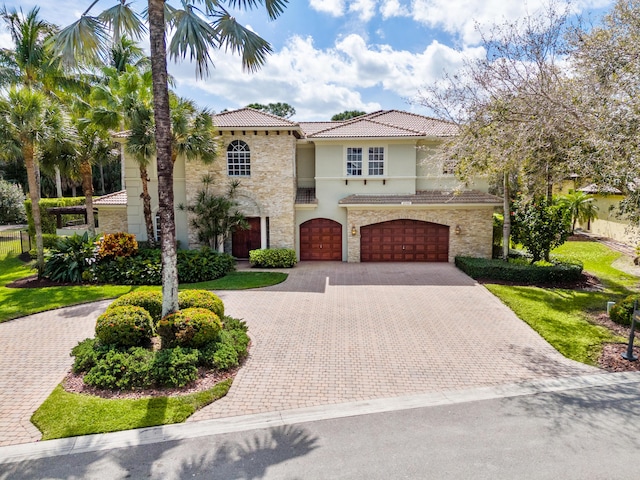 mediterranean / spanish-style house featuring stone siding, decorative driveway, an attached garage, and a tiled roof