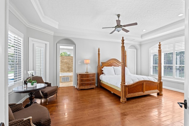 bedroom with a tray ceiling, crown molding, arched walkways, and hardwood / wood-style floors