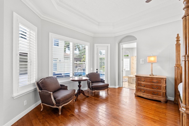 living area with light wood-style floors, a tray ceiling, crown molding, and baseboards