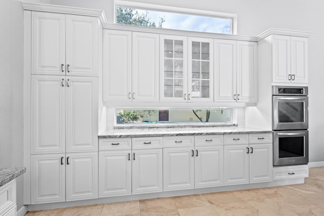 kitchen featuring double oven, light stone counters, glass insert cabinets, and white cabinetry