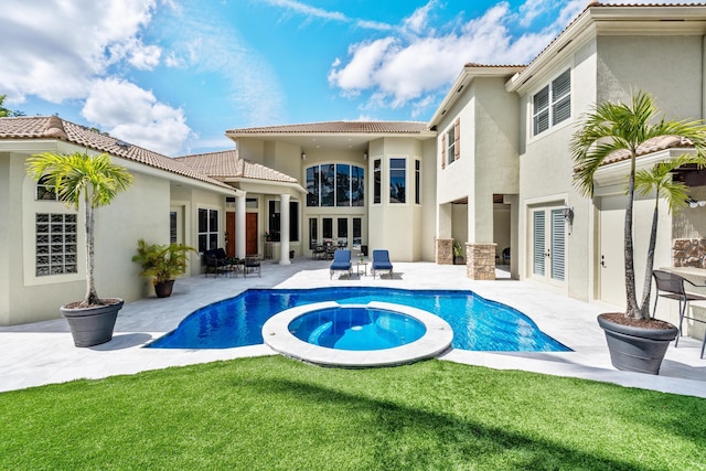 back of property with a patio, a tile roof, a pool with connected hot tub, a lawn, and stucco siding