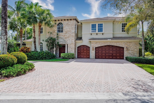 mediterranean / spanish-style home with stone siding, a tile roof, an attached garage, decorative driveway, and stucco siding