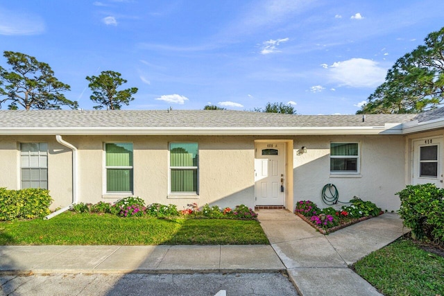 view of front of house featuring roof with shingles, a front lawn, and stucco siding