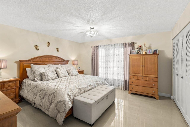 bedroom featuring a closet, a textured ceiling, baseboards, and light tile patterned floors