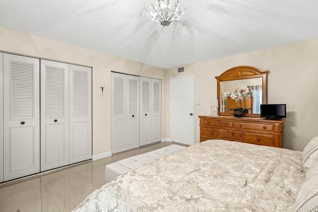 bedroom with a textured ceiling, tile patterned floors, visible vents, and multiple closets