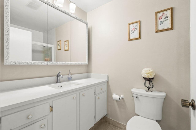 bathroom featuring baseboards, visible vents, toilet, a shower with shower door, and vanity