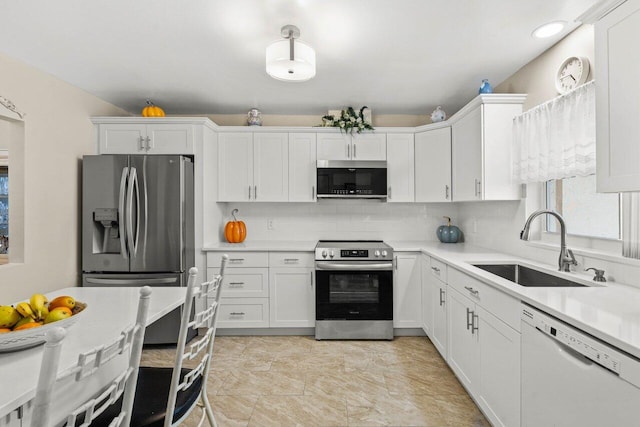 kitchen featuring stainless steel appliances, a sink, white cabinetry, light countertops, and decorative backsplash