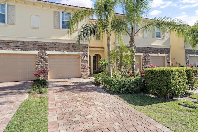 view of front facade with decorative driveway, stone siding, an attached garage, and stucco siding